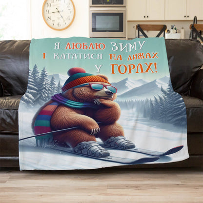 Плед із бурим ведмедем у шапці з помпоном, окулярах і шарфі на лижах серед засніжених гір, плед в інтер’єрі
