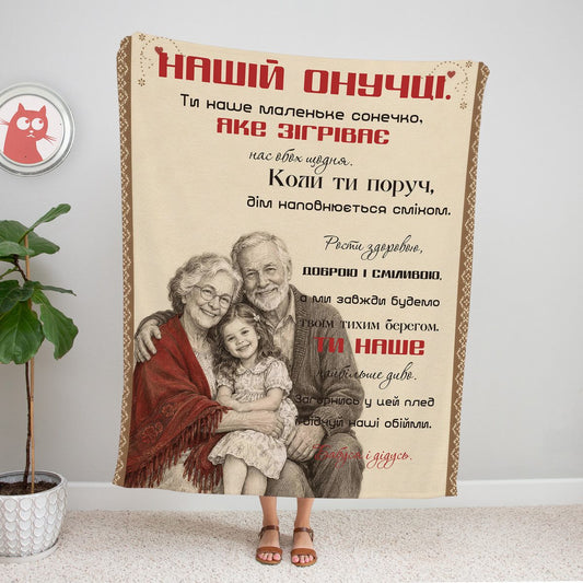 Плед-лист «Нашій онучці»: олівцева ілюстрація бабусі й дідуся з онучкою на колінах, червона хустка, орнаментна рамка